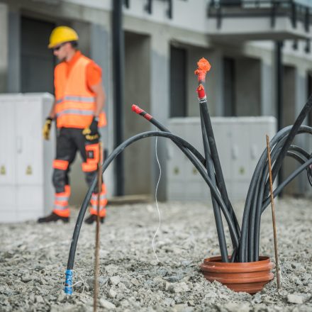 High Voltage Cables Installation. Bunch of Cables Comping From Underground Pipeline. Electric Technician in the Background.